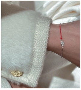 Detail of red string and silver chain bracelet with a single round cut zircon on wrist
