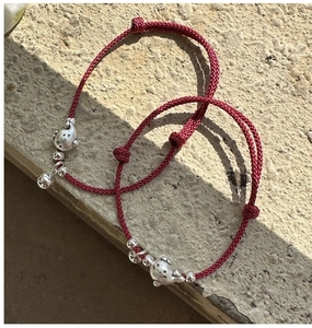 Détail de bracelets tressés rouges avec breloques de porcelets et nœuds ajustables