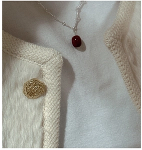 Detail of S925 silver necklace with red bean pendant on a cream coat outfit