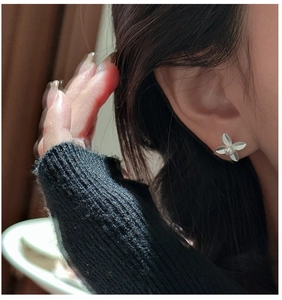 Close-up of matte silver flower stud earrings with a pearl center worn on a model