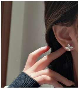 Close-up of minimalist four-leaf clover stud earring with silver finish on a model's ear