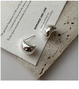 Macro shot of polished S925 silver curved stud earrings on a minimalist stone plate