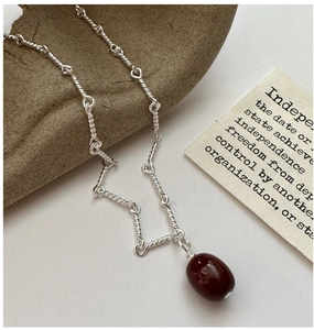 Detail of silver twisted chain necklace featuring a polished deep red bean pendant