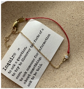 Detail view of red string bracelet with gold chain and sparkling round white zircon