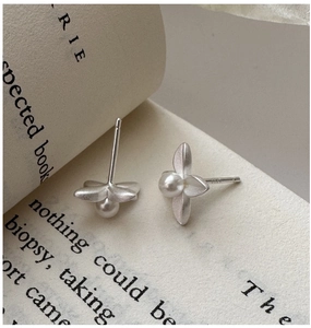 Close-up of matte S925 silver flower stud earrings with a white pearl center on a book