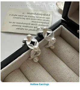 Detail of matte silver leaf earrings with shell pearls on a black leather jewelry box