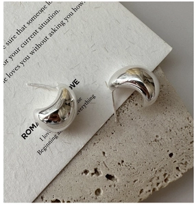 Macro detail of polished S925 sterling silver teardrop earrings on marble background