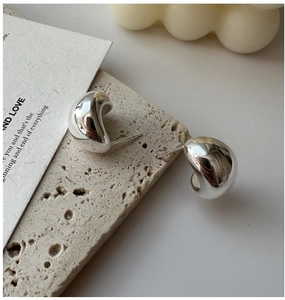 Macro shot of minimalist curved S925 sterling silver studs on a travertine stone base