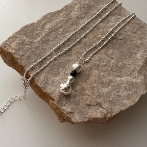 Collier artisanal en argent S925 avec perle noire posé sur une pierre naturelle