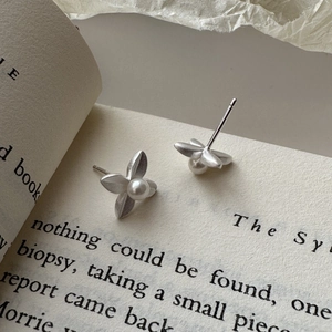 Matte silver leaf earrings with pearl centers on an open book background