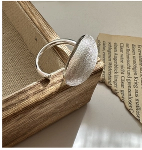 Gros plan d'une bague en argent S925 avec texture ovale brossée sur plateau bois