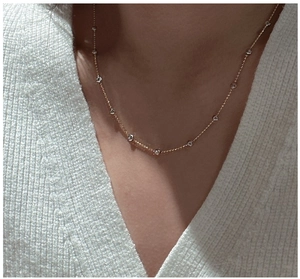 Detail of a minimalist gold necklace with round-cut crystals worn by a model over a white knit