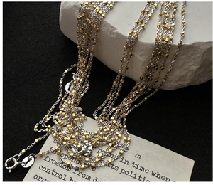 Detail of layered S925 silver necklace with gold square beads on textured stone