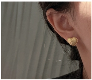 Close-up of brushed gold heart earrings with bead trim on a model ear lobe
