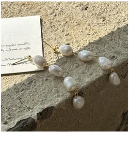 Detail view of long baroque pearl drop earrings with vintage gold finish on stone surface
