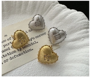 Detail of brushed silver and gold heart earrings with zircon clover on white fabric