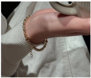 Detail of adjustable gold bead bracelet with lobster clasp on model's wrist with a cup