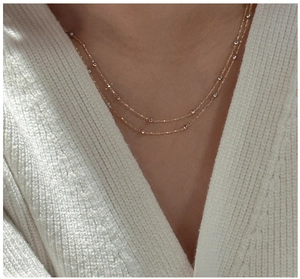 Gros plan d'un collier double épaisseur en argent S925 doré sur un pull en tricot blanc