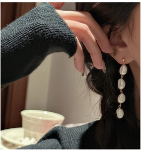 Detail of elegant baroque pearl drop earrings with gold chain worn by a model