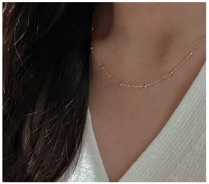 Détail d'un collier doré fin avec perles rondes porté sur un pull en maille blanc