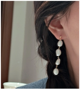 Detail of four baroque pearls on a gold drop earring worn by a model in soft light