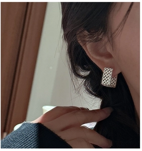 Gros plan sur des boucles d'oreilles tressées en argent portées par un mannequin femme