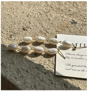 Detailed shot of baroque pearl drop earrings with gold chains on stone surface