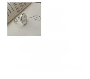 Close-up of S925 sterling silver floral ring with oval engraved flower on vintage book