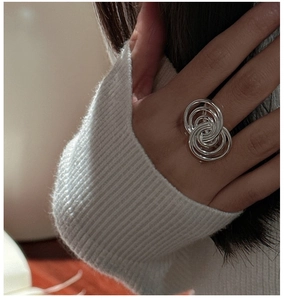 Detail of multi-layered silver interlaced ring worn over a white knitted sleeve