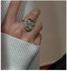 Close-up of a silver retro flower-engraved signet ring worn by a model in a knit sweater