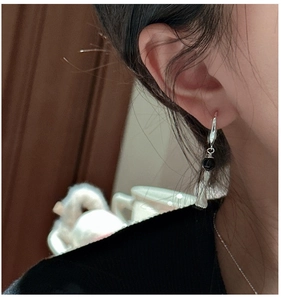 Detail of S925 silver earring with a black bead and textured broom pendant on a model