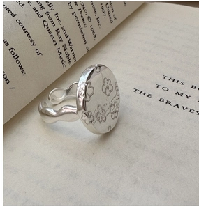 Close-up of S925 sterling silver flower ring with vintage wavy band on an open book
