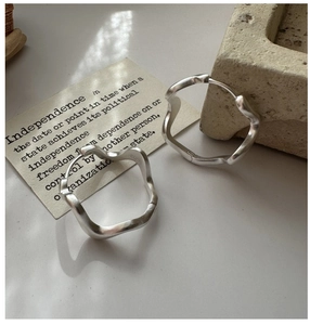 Macro detail showing matte S925 sterling silver wavy hoop earrings with hallmark