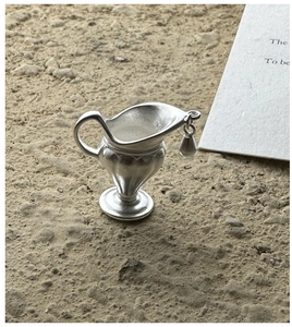Macro shot of silver matte flask pendant with relief lines on a textured stone surface