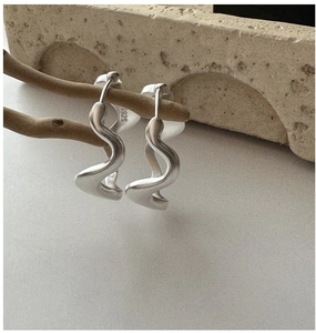 Macro view of S925 sterling silver earrings with wavy texture and matte finish on wood
