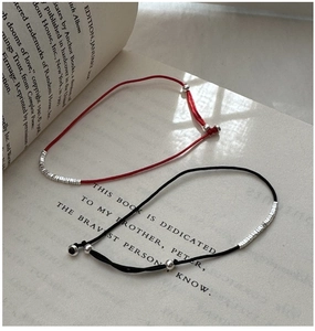 Close-up of red and black cord bracelets with silver beads on a vintage book page
