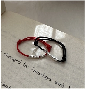 Macro shot of minimalist red and black woven cord rings with silver hex beads on a book