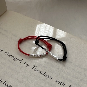 Minimalist red and black woven cord rings with adjustable silver bead design on a book
