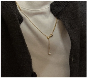 Close-up of golden ball chain necklace with a single zircon pendant worn on neck