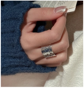 Gros plan d'une bague large en argent S925 avec texture martelée et reflets métalliques