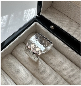 Détail macro d'une bague large argentée à texture martelée dans un écrin de luxe