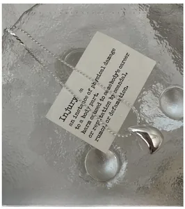 Détail macro du pendentif goutte d'eau argenté sur un plateau en verre texturé