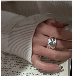 Detailed view of silver multi-layer ripple ring worn on hand over a book