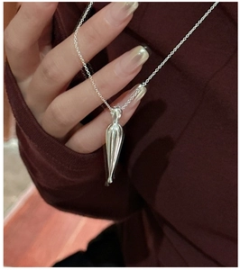 Macro shot of silver teardrop pendant necklace on red sweater showing the drop effect
