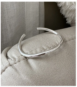 Macro shot of minimalist S925 sterling silver cuff bracelet on a beige leather texture