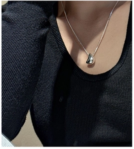 Détail d'un pendentif goutte en argent poli sur une chaîne fine portée sur un pull
