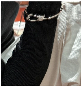 Close-up of a silver knot open bangle featuring a U-shaped hook clasp on a black sleeve