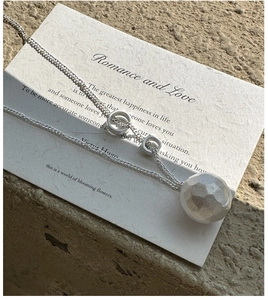 Macro detail of textured silver sphere pendant and dainty chain on aesthetic paper