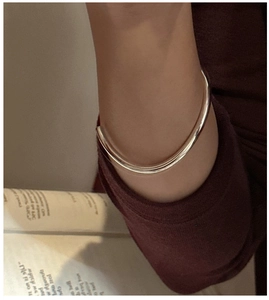 Minimalist silver open cuff bracelet styled on a wrist with a dark red sweater background