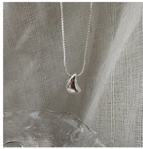 Gros plan d'un collier avec pendentif goutte en argent poli sur fond de tissu texturé